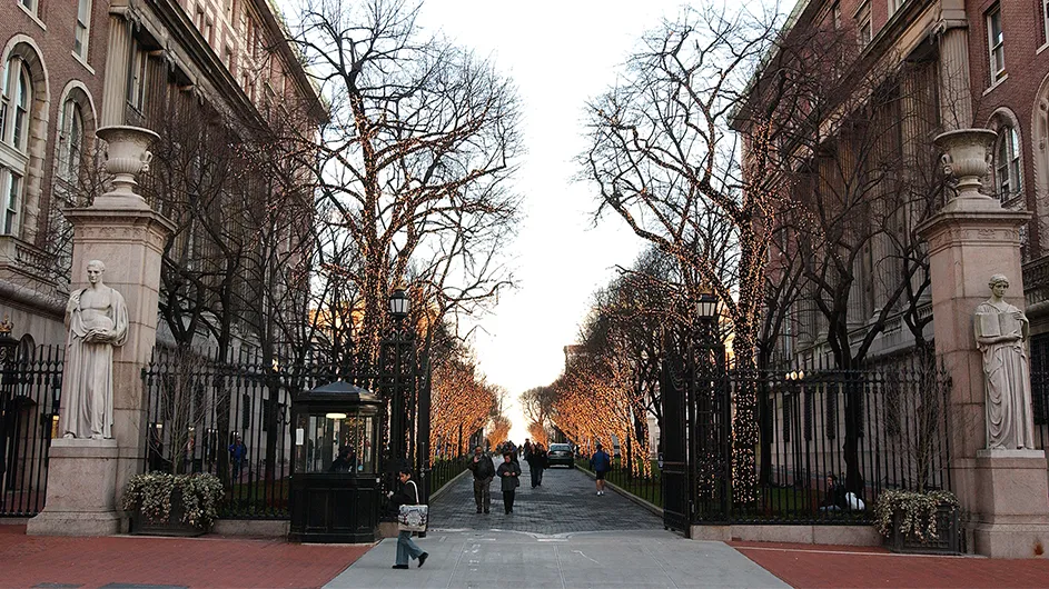 Two pylons on either side of the 116th gates beckon those who enter with the Latin inscriptions "Scientia" and "Hic Labor, Haec Quies." College Walk looms in the background.
