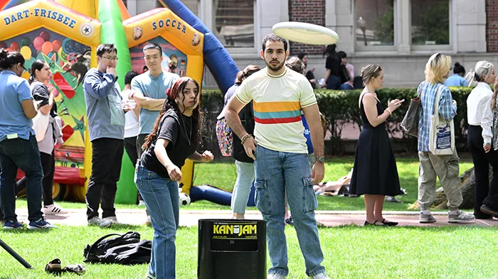 A student tosses a frisbee with a bounce house in the back ground.
