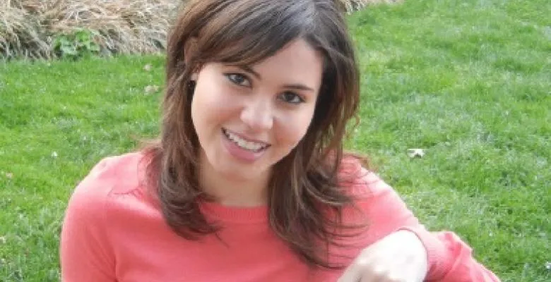 Young dark-haired woman smiling, wearing a pink sweater and sitting on a lawn