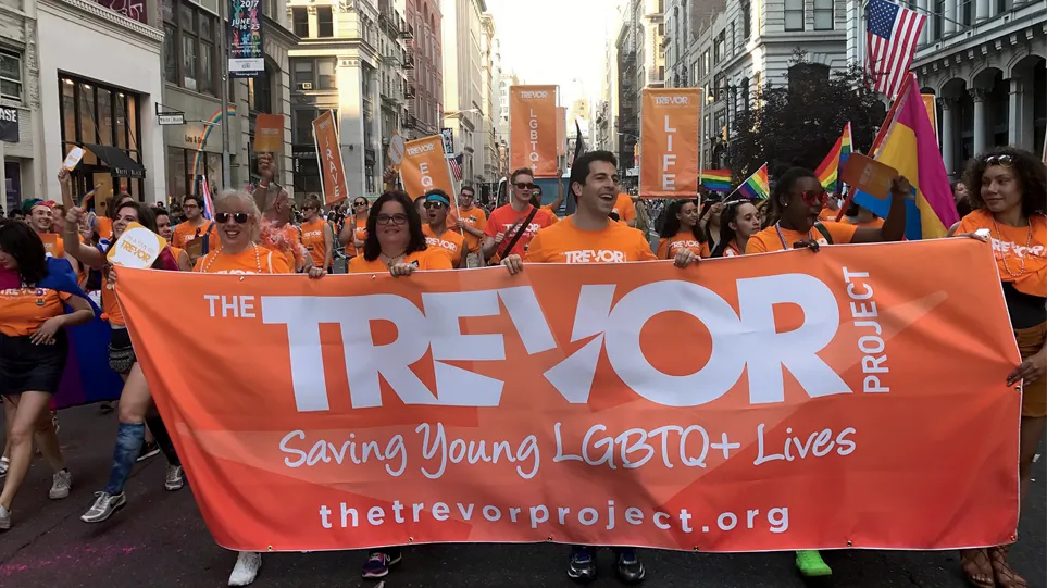 Members of the Trevor Project carrying an orange banner at a street march. 