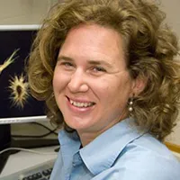 woman in light blue shirt with collar from shoulder up. Brown medium length curly hair smiling